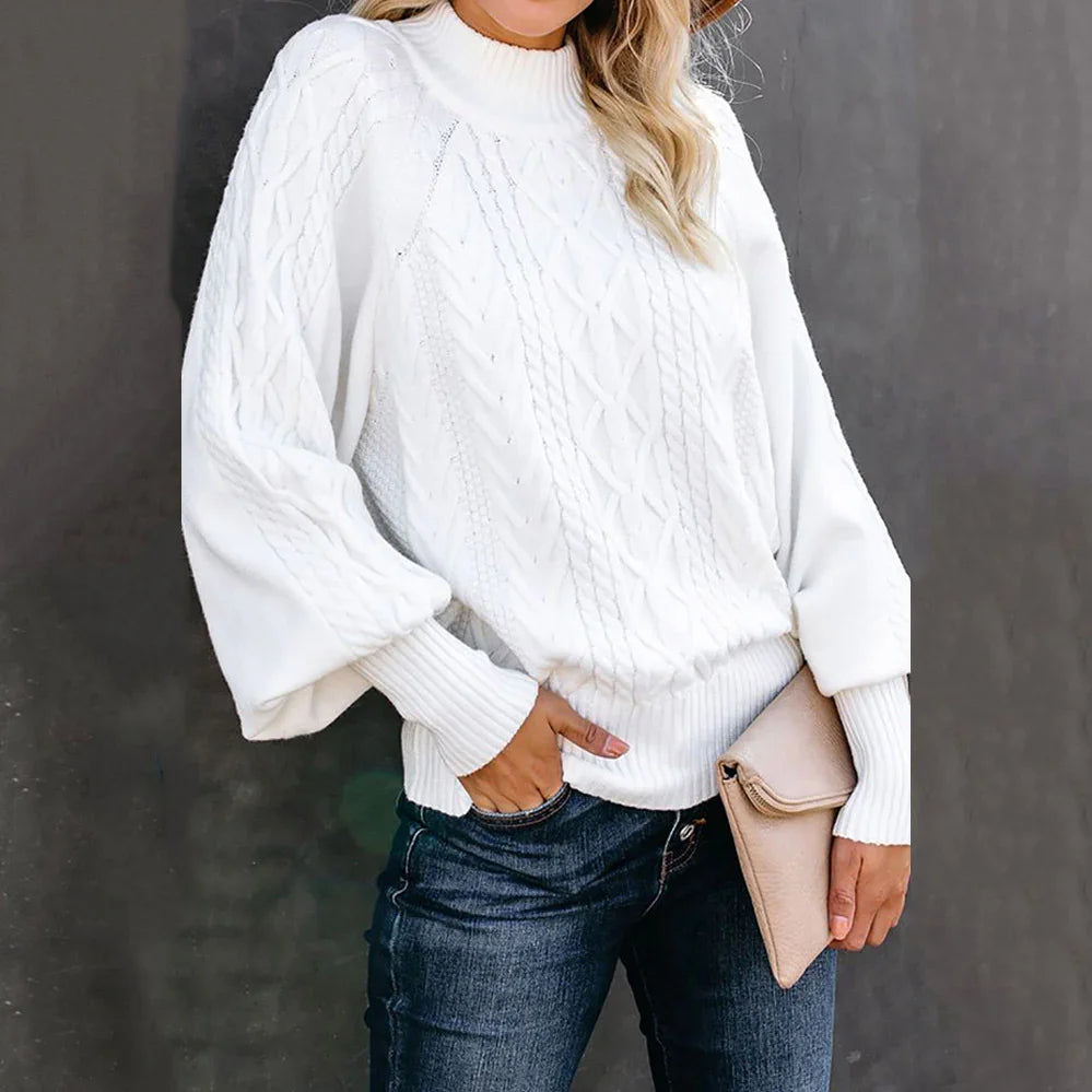 Woman wearing white cable knit sweater with balloon sleeves and dark jeans holding beige clutch