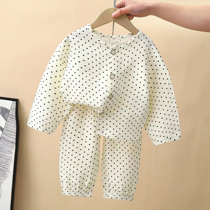 Hand holding a wooden hanger with white polka dot baby pajama set featuring buttons