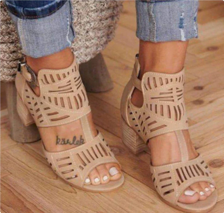 Beige cutout block heel sandals worn with rolled-up blue jeans on wooden floor