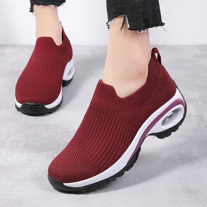 Maroon slip-on knit sneakers with white and black air-cushioned soles worn with black frayed hem jeans
