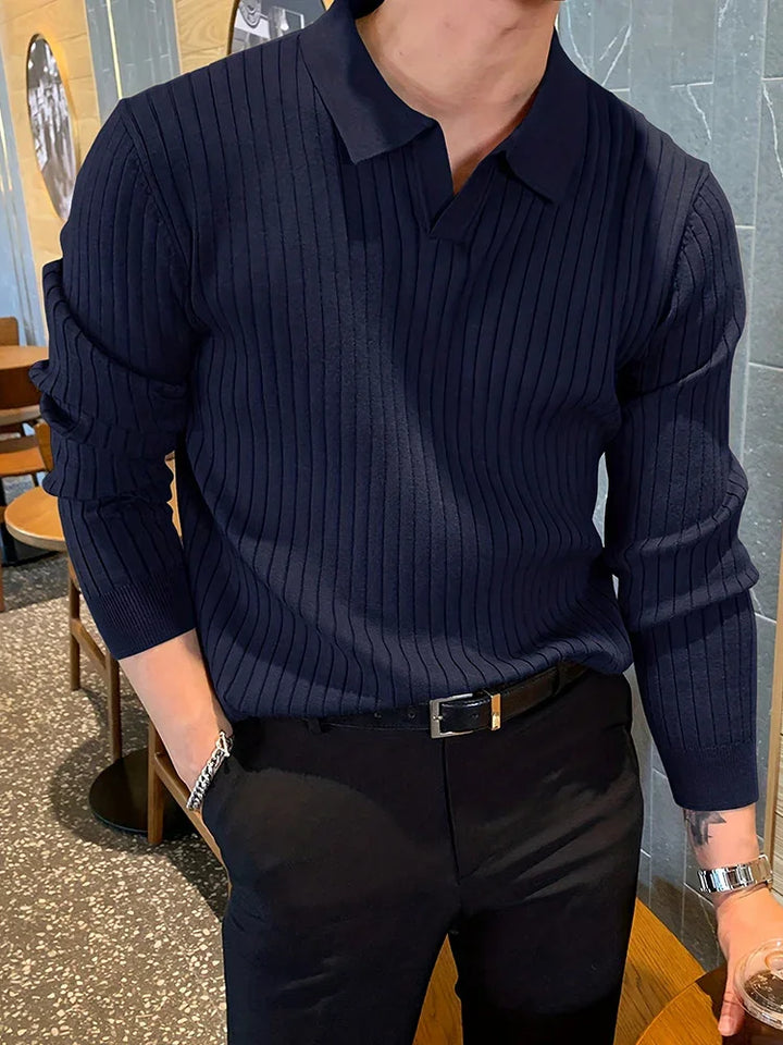 Man wearing a navy blue ribbed knit long sleeve polo shirt with black pants and a black belt in a cafe setting