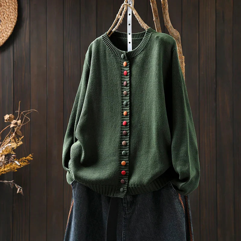 Dark green knitted cardigan with colorful buttons hanging on wooden background
