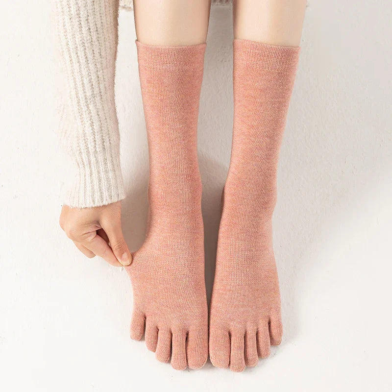 Person wearing pink toe socks stretching fabric on one foot, white knitted sweater sleeve visible