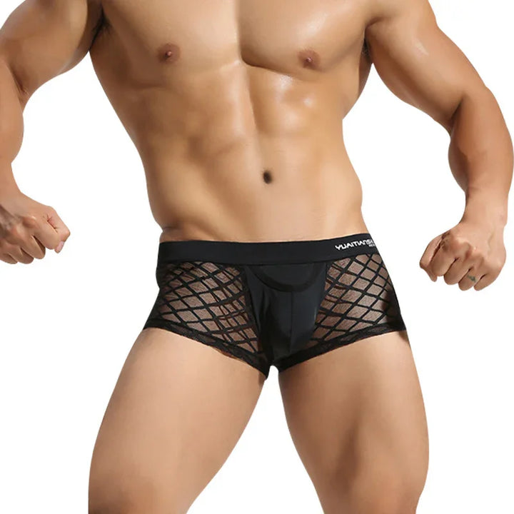 Fit male model wearing black mesh boxer briefs with a geometric pattern on a white background