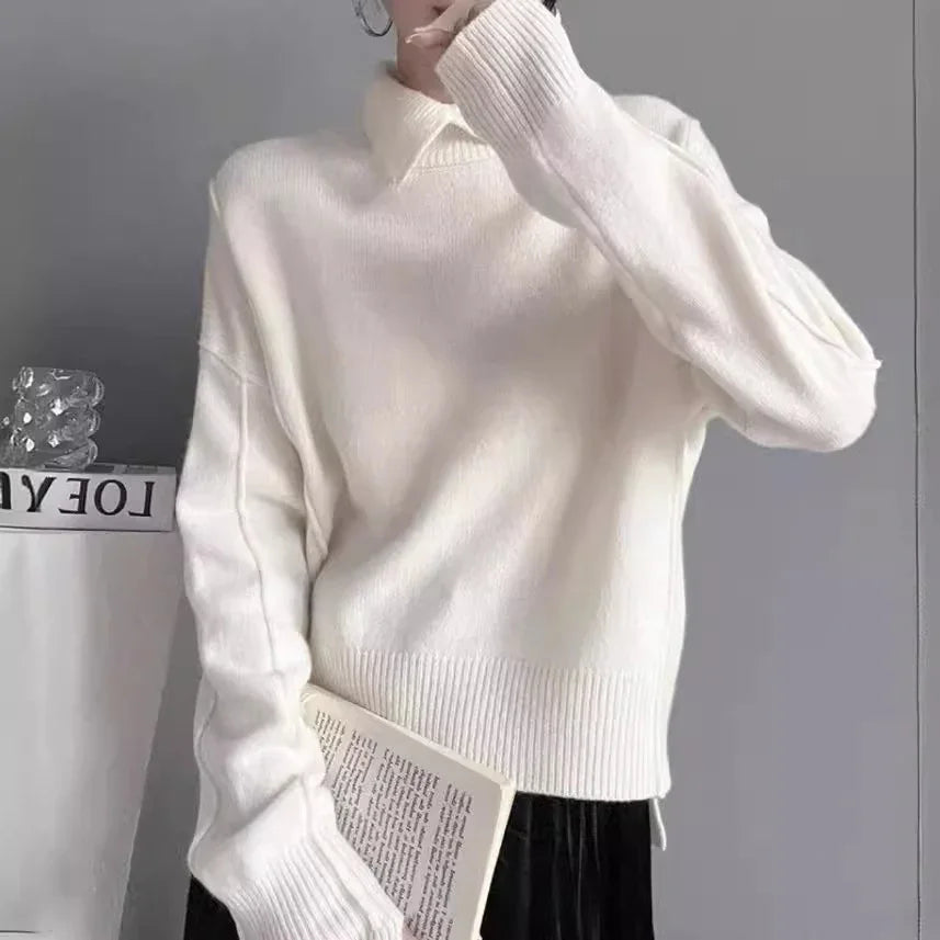 Person wearing off-white knit sweater holding an open book against gray background