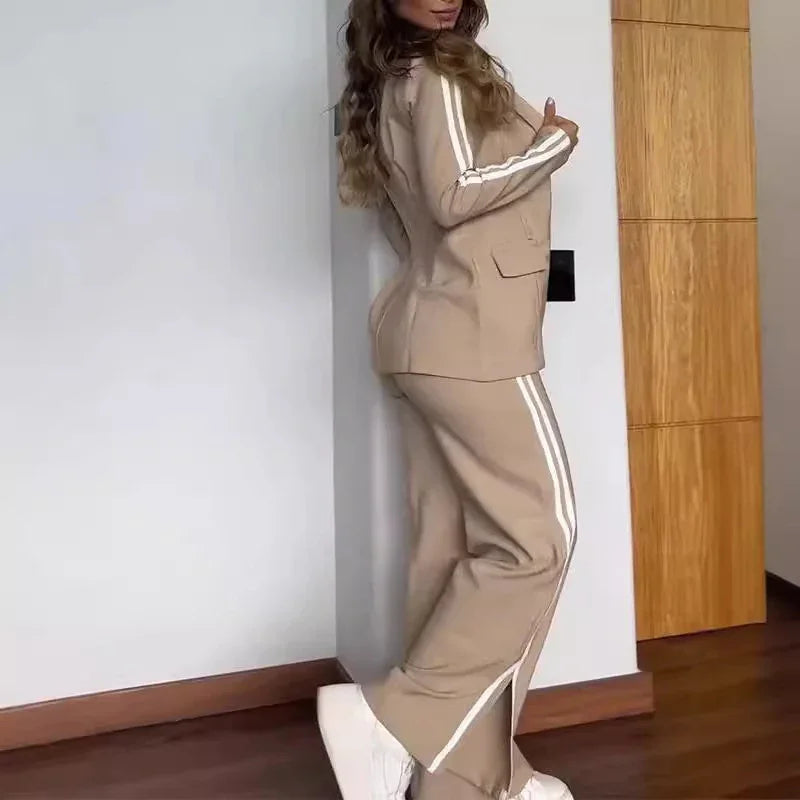 Woman wearing beige two-piece suit with white stripes on sleeves and pants, posing indoors on wooden floor