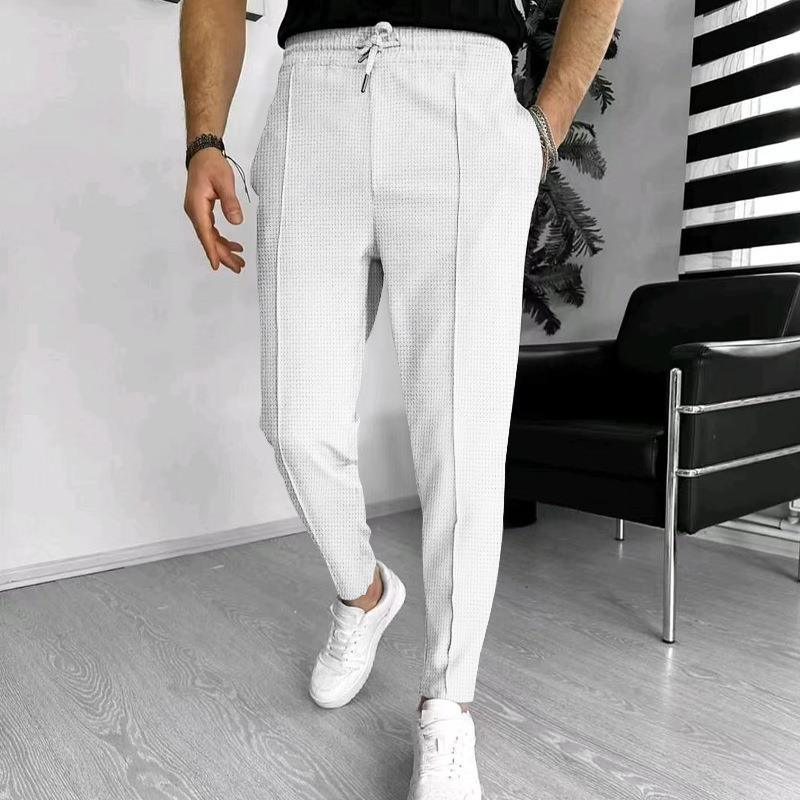 Man wearing white drawstring jogger pants and white sneakers in modern room with black chair