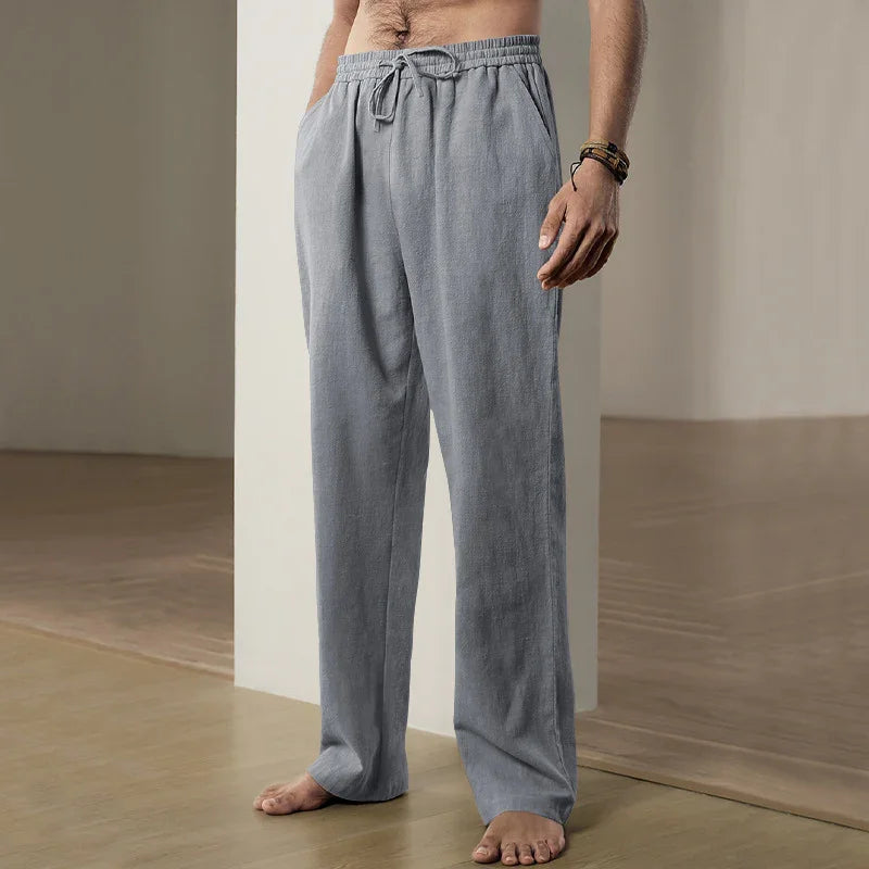 Man wearing loose grey sweatpants with drawstring, standing barefoot on wooden floor indoors