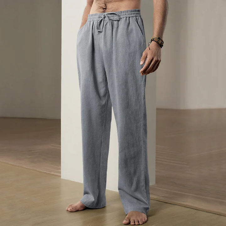 Man wearing loose grey sweatpants with drawstring, standing barefoot on wooden floor indoors