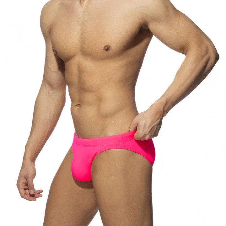 Muscular male torso wearing bright pink swim briefs against white background