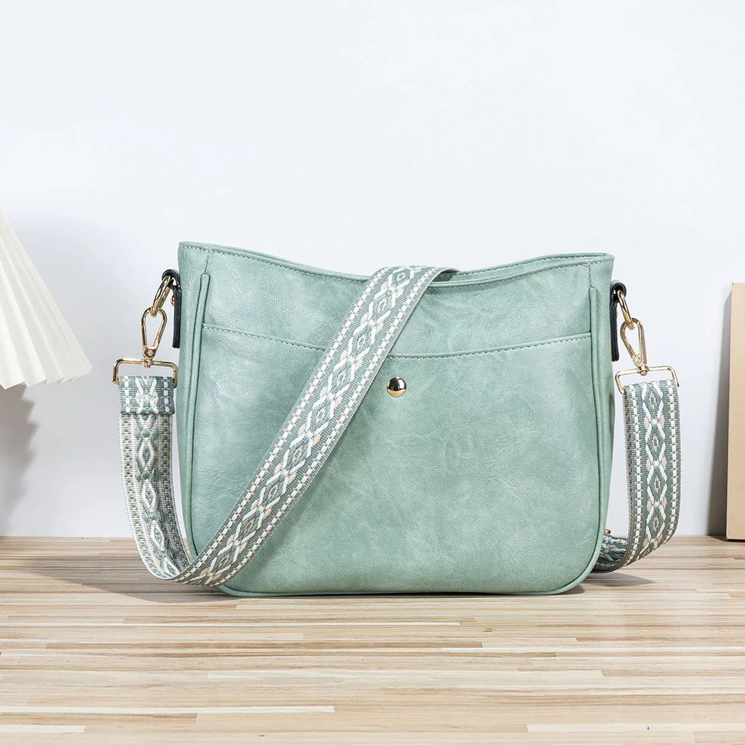 Mint green crossbody bag with patterned adjustable strap on wooden surface