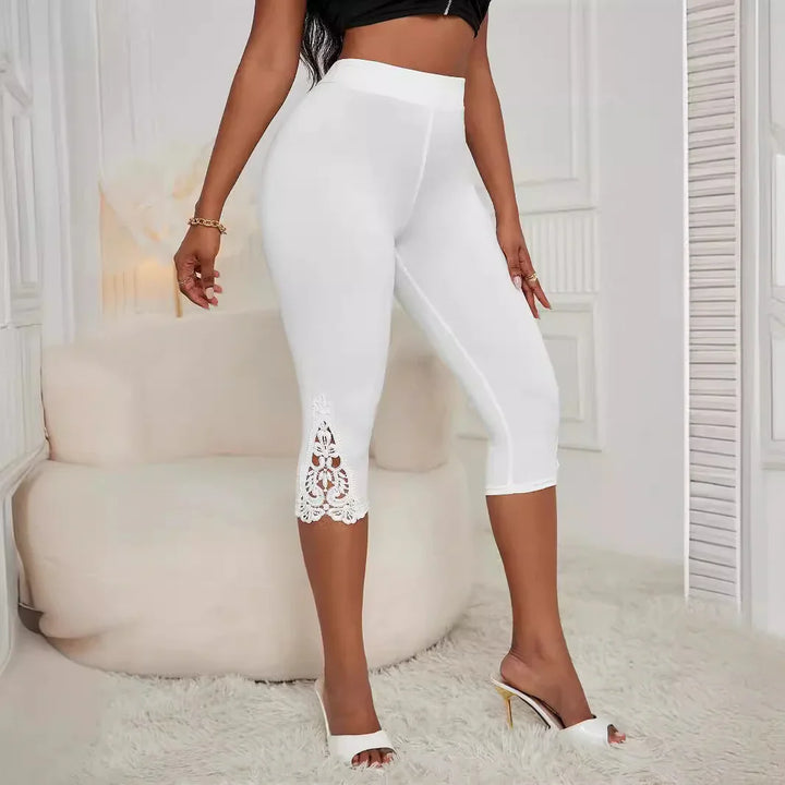 Woman wearing white capri leggings with lace cutout detail and white heeled sandals in modern room