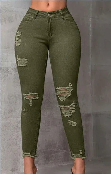 Woman wearing olive green distressed skinny jeans with ripped details and frayed hems against a gray wall