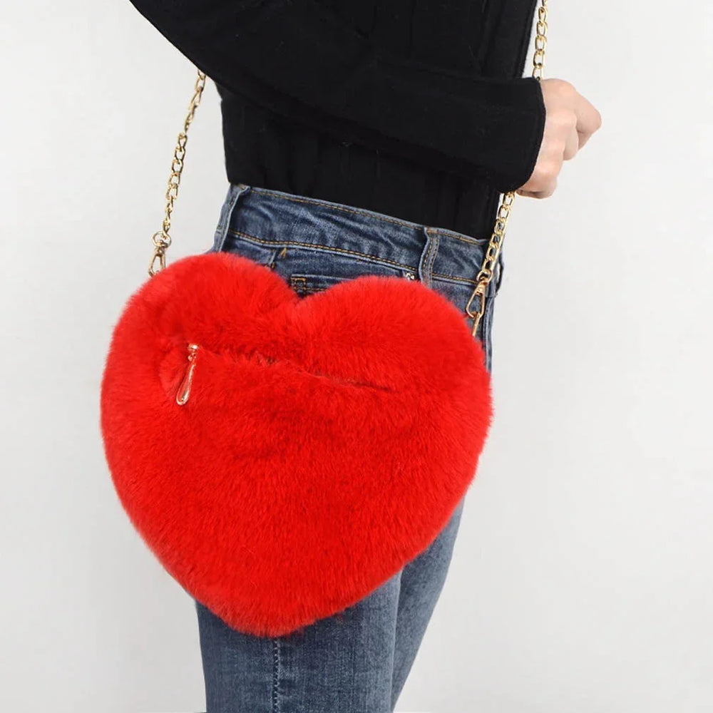 Red fluffy heart-shaped crossbody bag with gold chain strap worn with black top and jeans