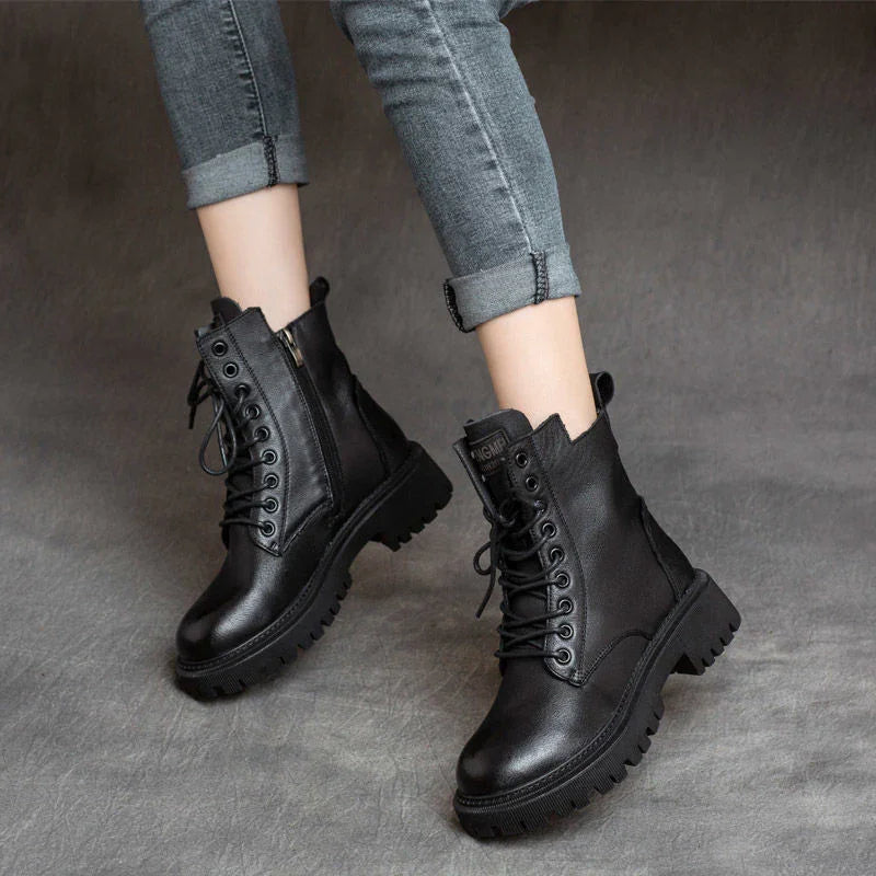 Black leather lace-up combat boots worn with rolled-up gray denim jeans on gray floor