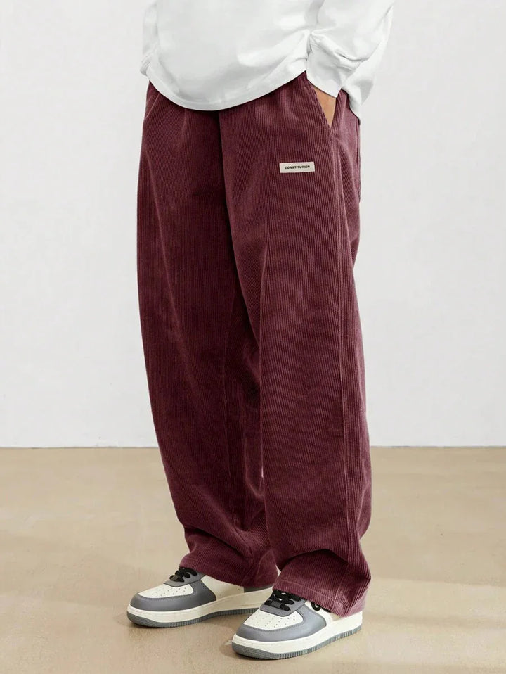 Person wearing loose maroon corduroy pants with white sneakers on beige floor