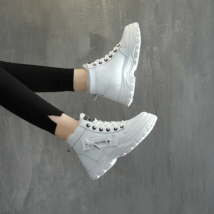 White high-top boots with black eyelets and text detail worn with black leggings against gray background