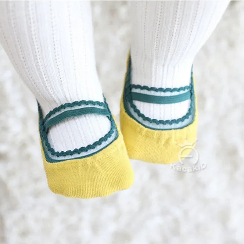 Close-up of baby feet wearing white socks with yellow and green ballet shoe design on a soft white textured surface