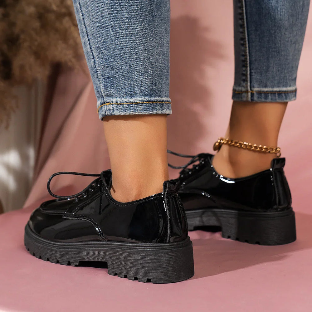 Woman wearing black patent leather platform shoes with thick soles and rolled blue jeans