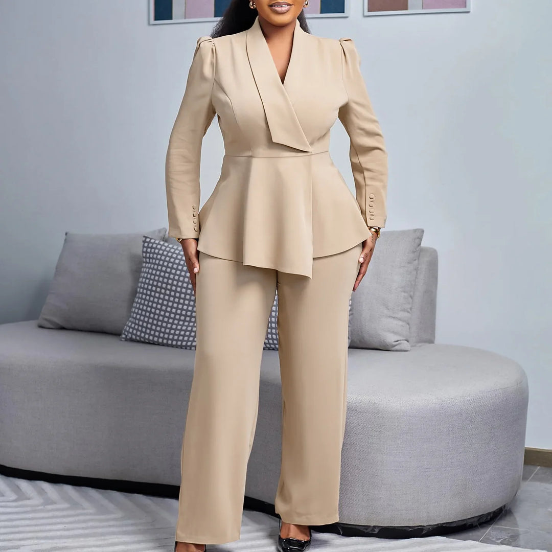 Woman wearing beige stylish pantsuit with asymmetrical blazer standing in modern living room