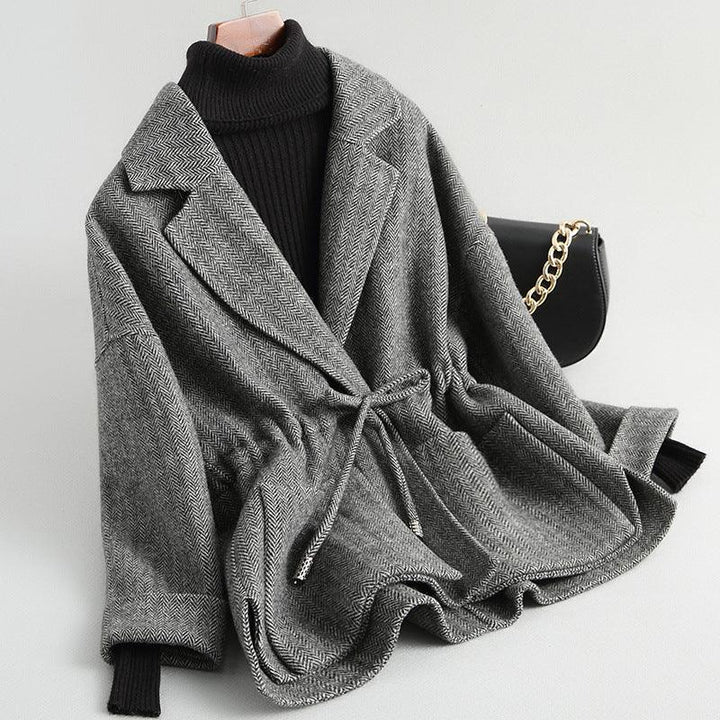 Gray herringbone wrap coat with tie waist over black turtleneck sweater next to black handbag with gold chain