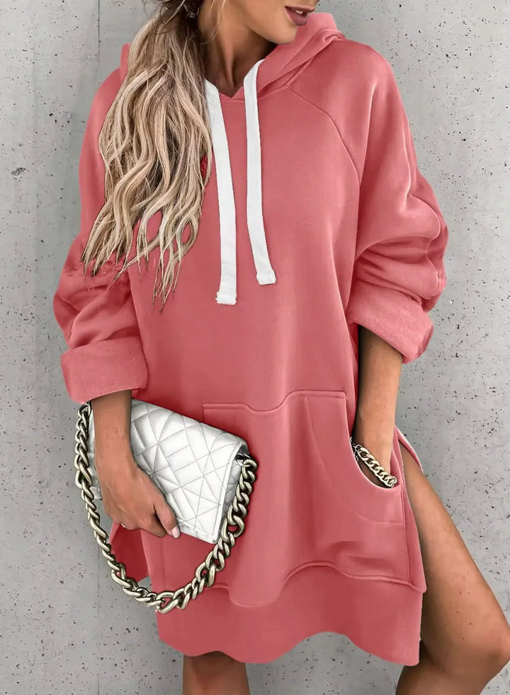 Woman wearing oversized pink hoodie dress with white drawstrings, holding quilted white purse with chunky chain strap
