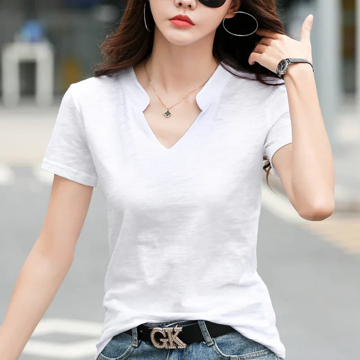 Woman wearing white v-neck t-shirt, blue jeans with GK belt, sunglasses, watch, and hoop earrings