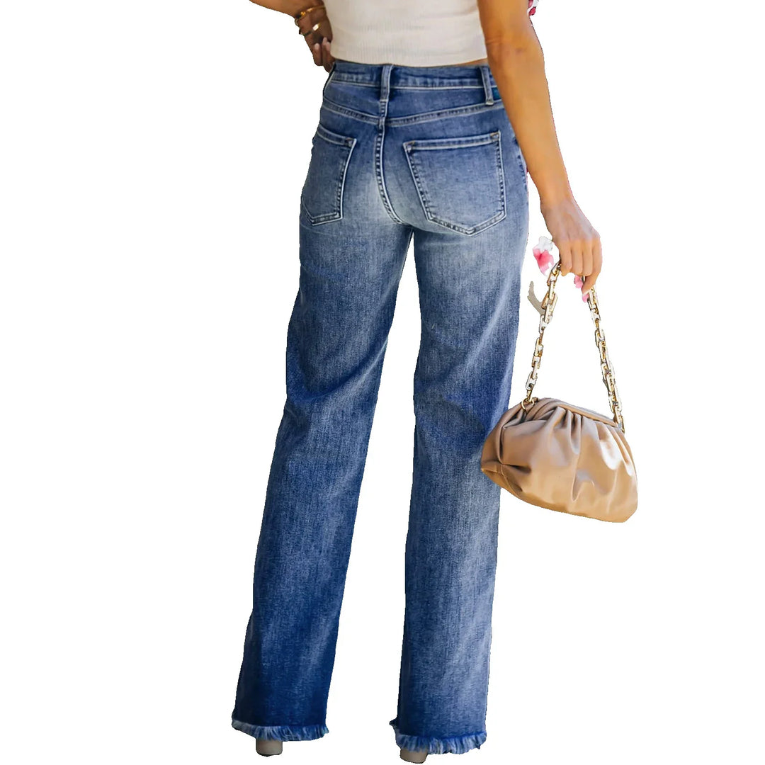 Back view of woman wearing high-waisted blue denim jeans with frayed hems holding beige handbag