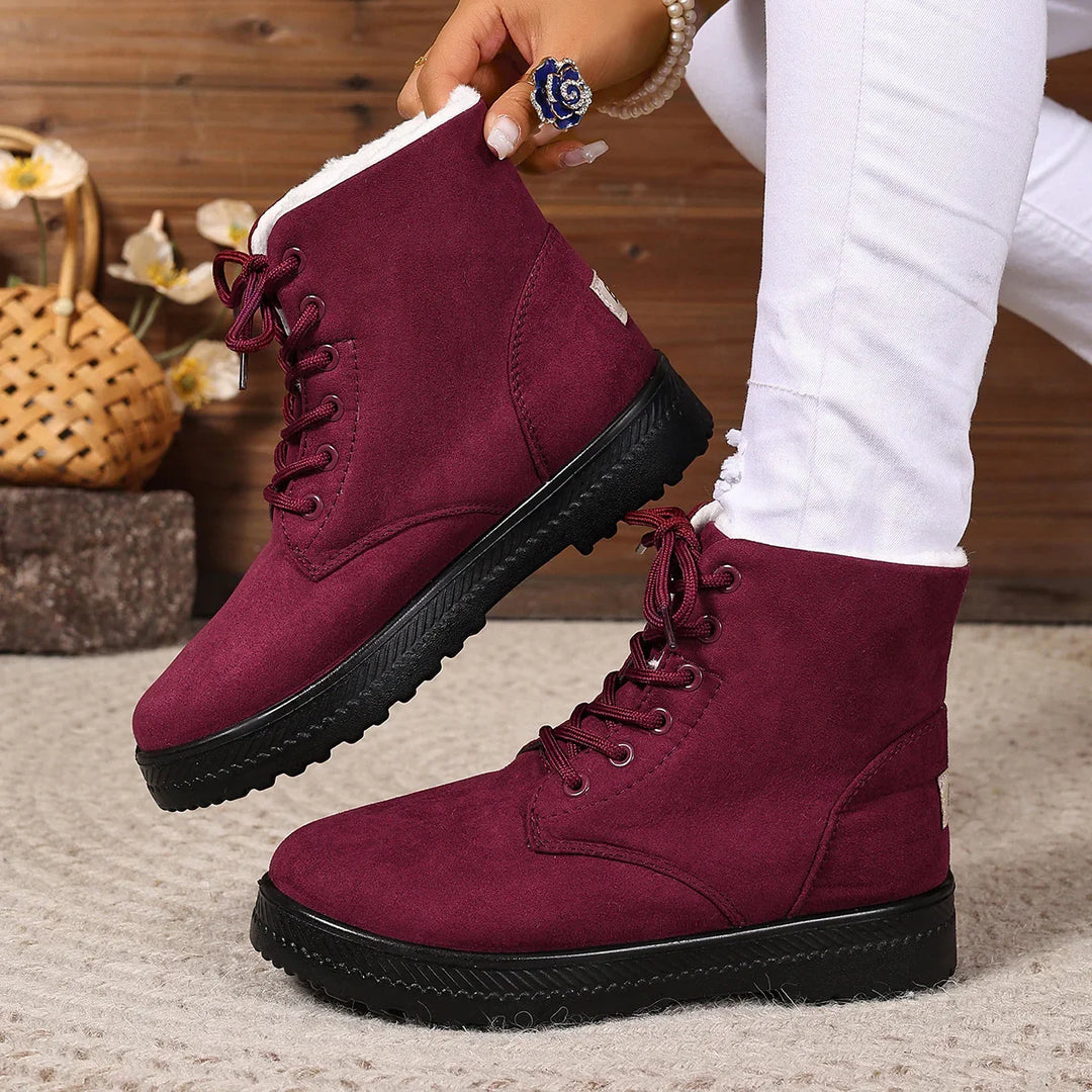 Women's burgundy winter boots with black soles and white fleece lining worn with white pants