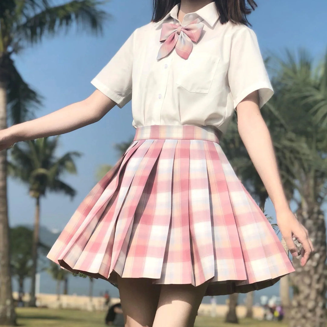 Woman wearing white blouse with pink plaid bow and matching pleated skirt outdoors with palm trees