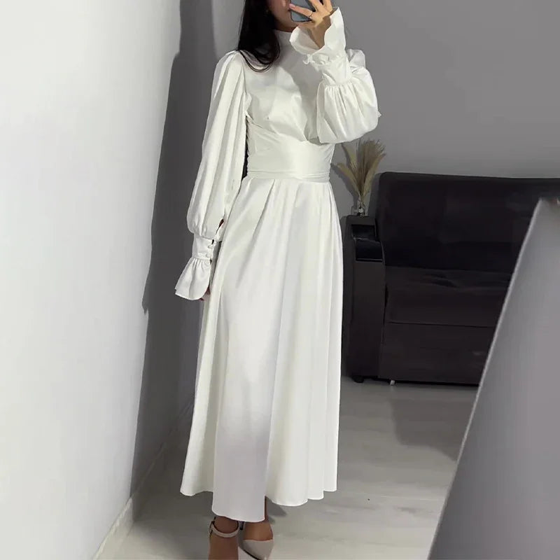 Woman in a white long-sleeve, high-neck midi dress with puffed sleeves taking mirror selfie indoors