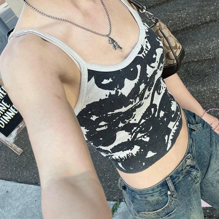 Person wearing black and white graphic tank top, blue jeans, silver necklace, and carrying brown Coach handbag