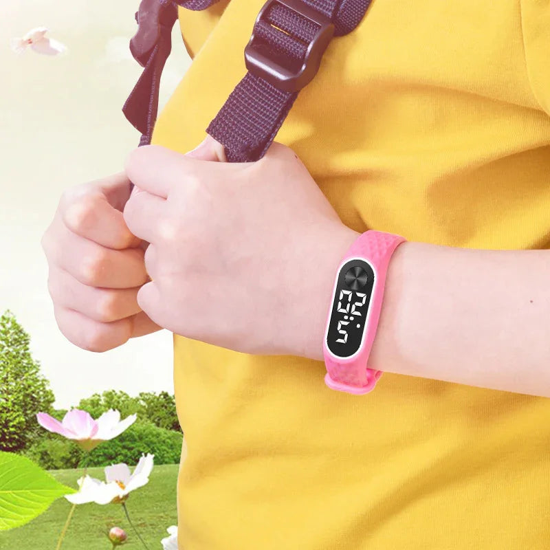 Child wearing pink digital watch with sport strap holding backpack straps outdoors near flowers