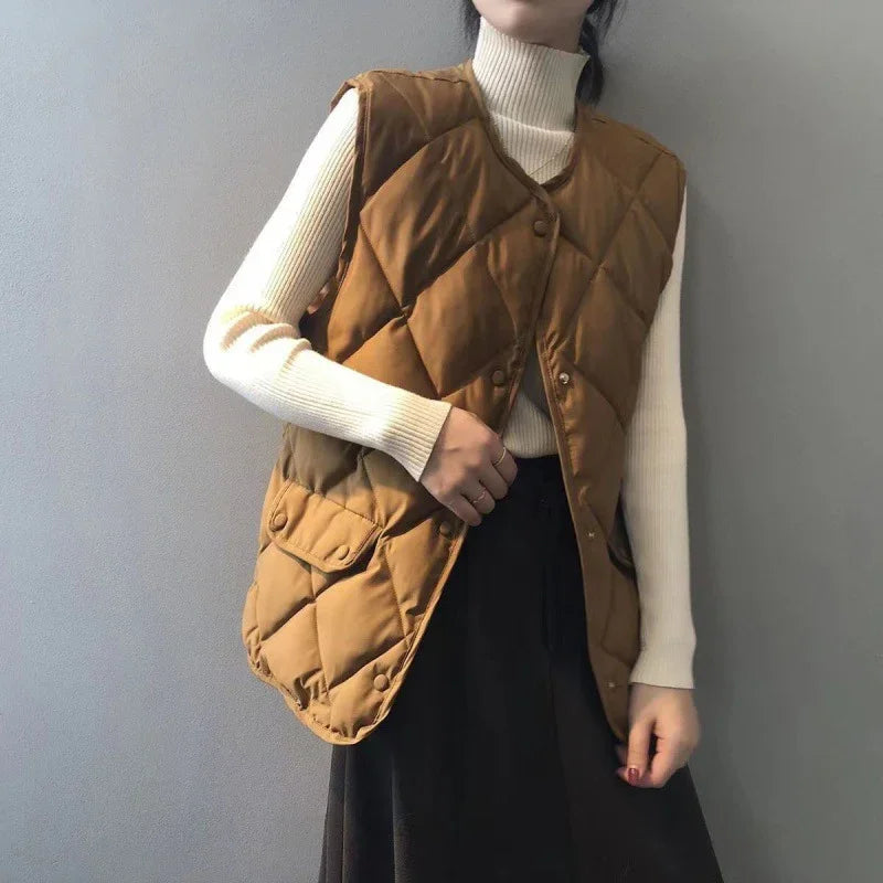 woman wearing brown quilted vest over cream turtleneck sweater and black skirt against gray background