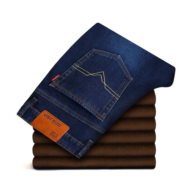 Folded dark blue denim jeans with contrast stitching and leather patch on brown fabric background