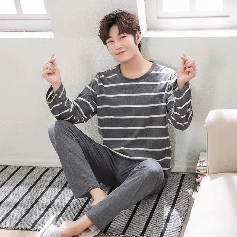 Young man sitting on striped rug wearing grey striped long-sleeve shirt and grey pants in bright room