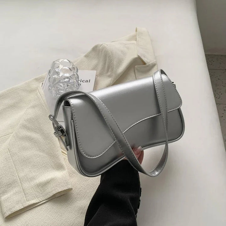 Hand holding a silver metallic leather shoulder bag over cream fabric and a textured outfit