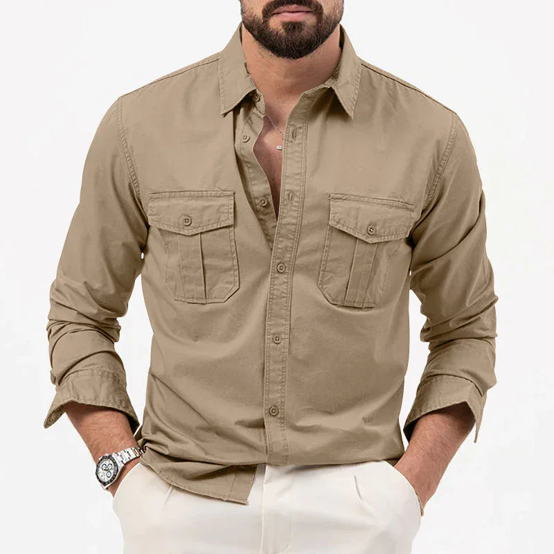 Man wearing beige casual button-up shirt with chest pockets and white pants, hands in pockets