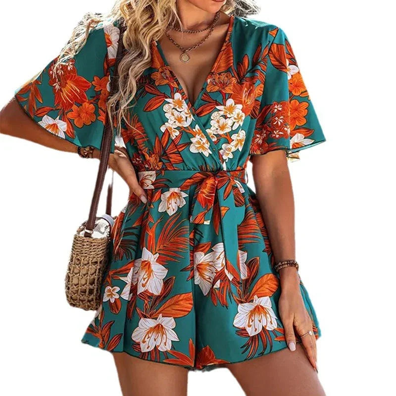 woman wearing green floral short sleeve romper with orange and white flowers, carrying woven shoulder bag