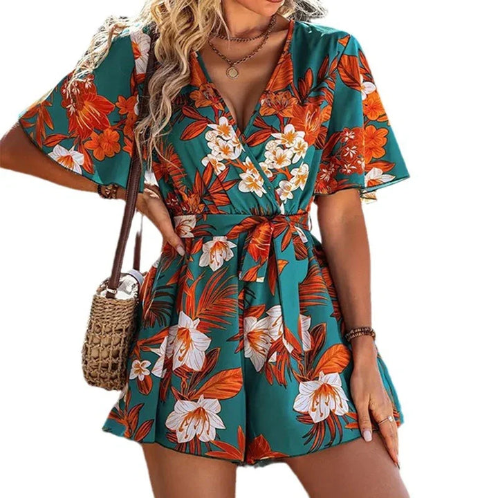 woman wearing green floral short sleeve romper with orange and white flowers, carrying woven shoulder bag