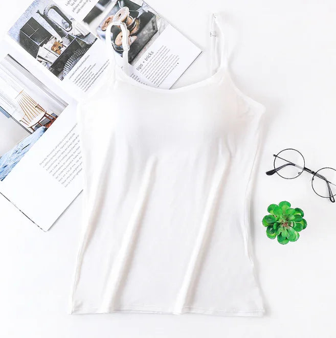 White sleeveless camisole top with adjustable straps, next to reading glasses, a small green succulent, and open magazines