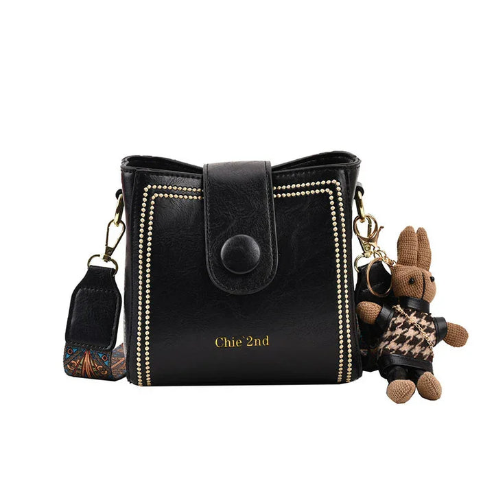 Black leather crossbody bag with gold stud detailing, detachable strap, and attached bunny keychain