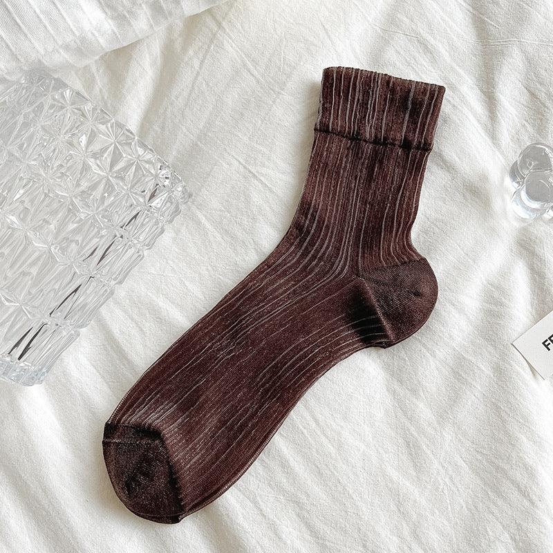 Dark brown ribbed crew sock on white fabric with glass decor nearby