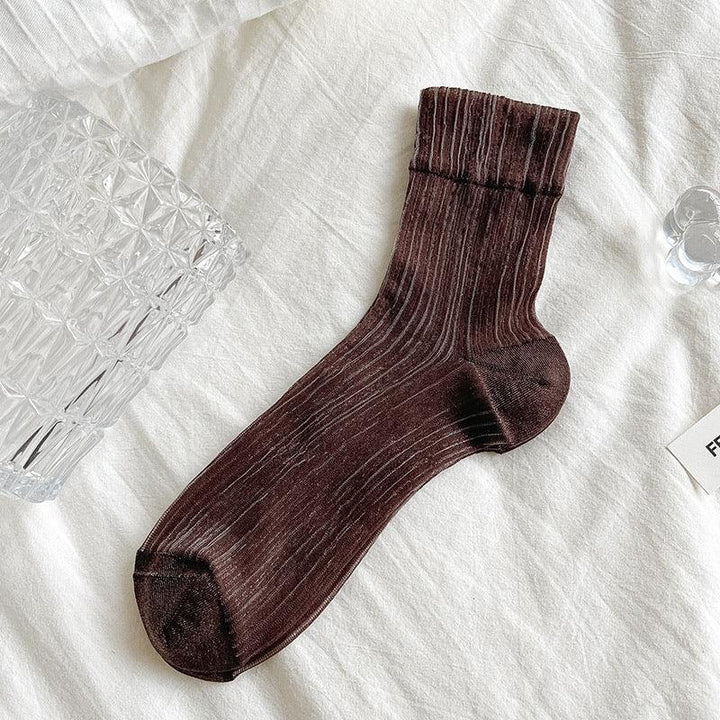 Dark brown ribbed crew sock on white fabric with glass decor nearby