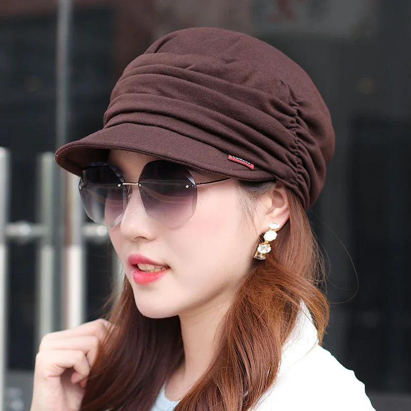 Woman wearing brown ruched cap, large sunglasses, and drop earrings with white and gold details