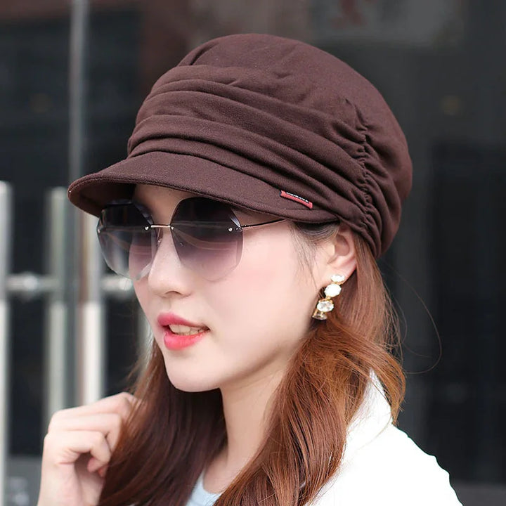 Woman wearing brown ruched cap, large sunglasses, and drop earrings with white and gold details