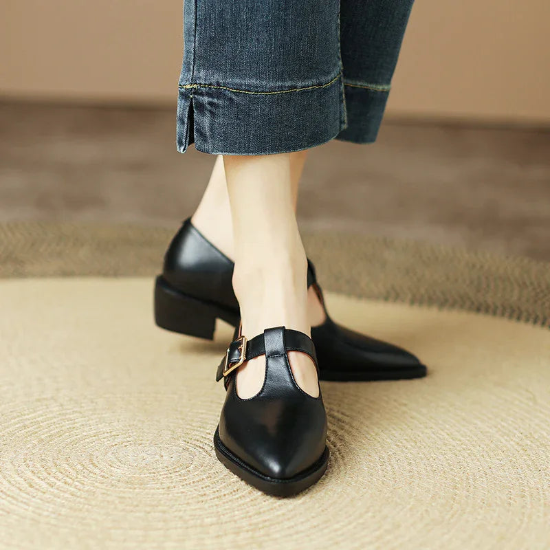 Close-up of black leather T-strap pointed-toe shoes with buckle, worn with cropped denim jeans