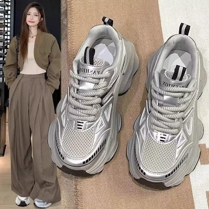 Chunky silver mesh sneakers with thick soles on beige and white fabric next to woman in brown wide pants and jacket