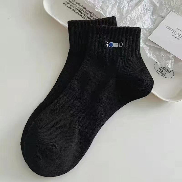 Pair of black ankle socks with ribbed cuffs and 'GOOD' embroidery on white tray