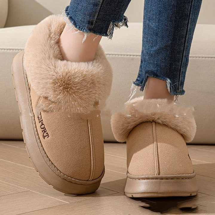 Beige faux fur-lined winter slippers with sport embroidery worn with frayed blue jeans on wooden floor